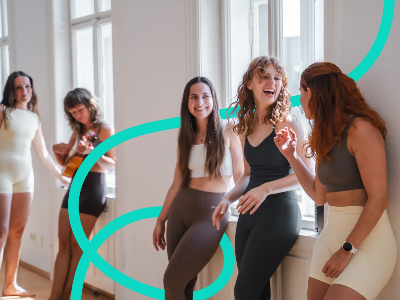 Vier Frauen in Sportkleidung unterhalten sich und lachen vor sonnenbeschienenen Fenstern vor dem Unterricht..