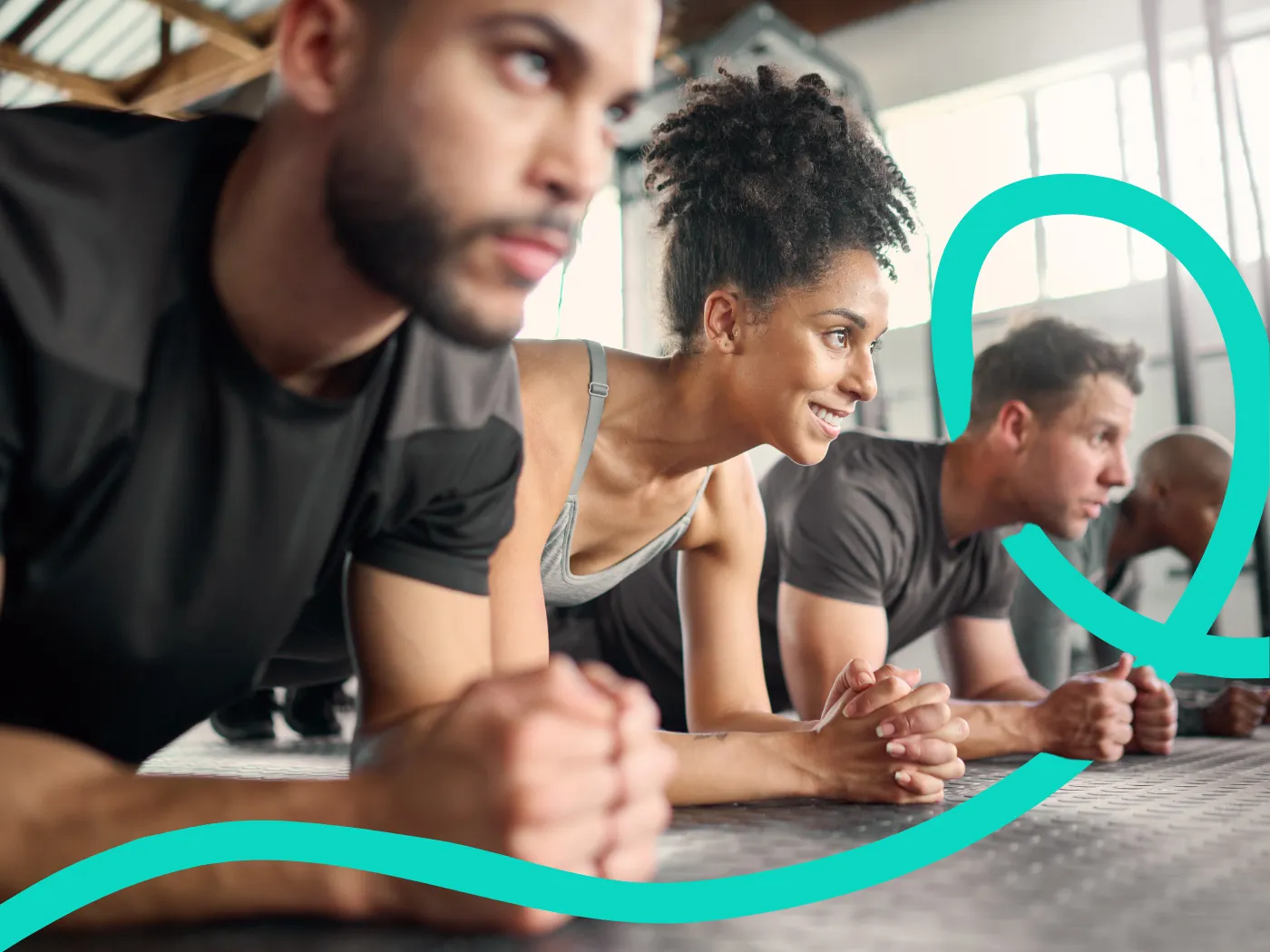 Vier Personen sitzen auf dem Boden eines Fitnessstudios, lächeln und unterhalten sich, im Hintergrund sind Trainingsgeräte und große Fenster zu sehen.