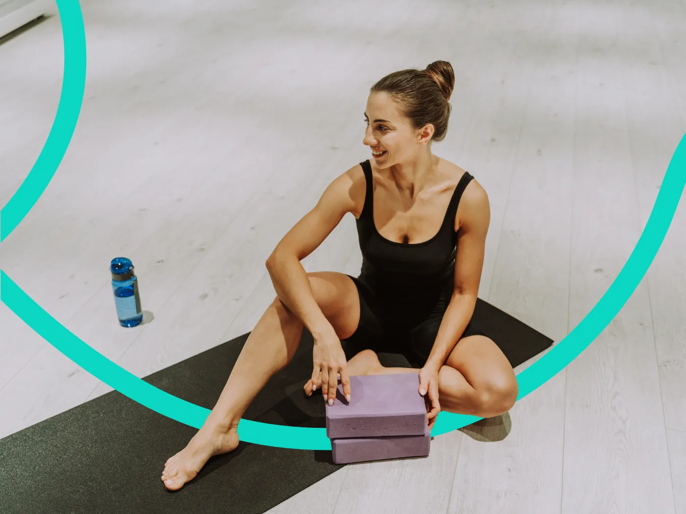 Frau in Sportkleidung sitzt auf einer Yogamatte und hält einen Yogablock.