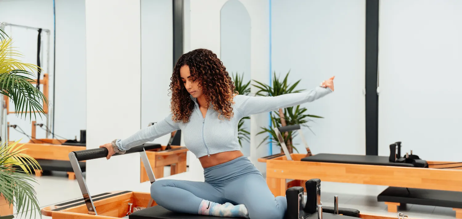 Junge Dame auf Reformer Maschine macht Pilates Übrungen.