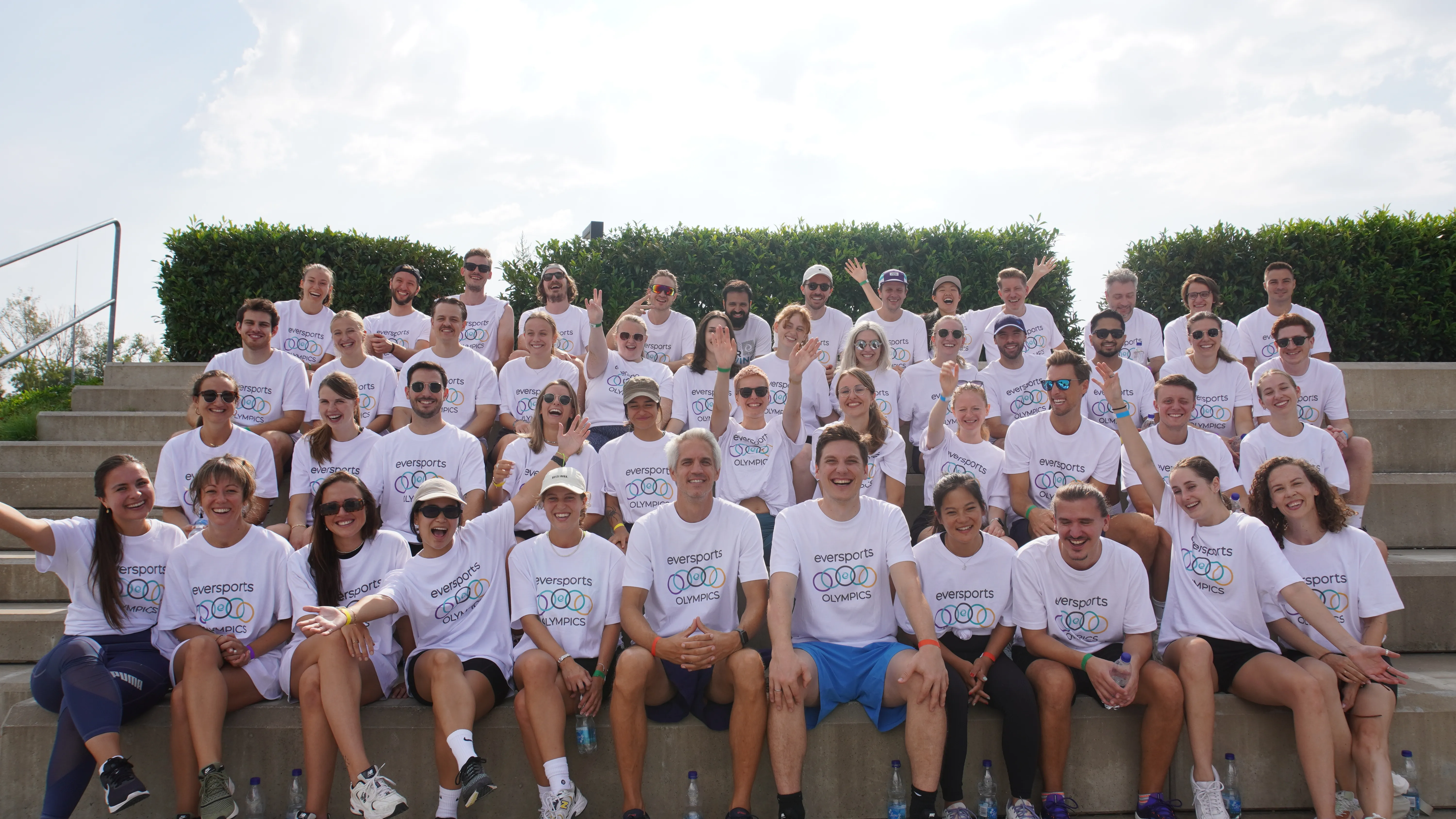 Das Eversports-Team in passenden Marken-Shirts lächelt gemeinsam auf dem jährlichen Sommerausflug, wir sind dein Partner