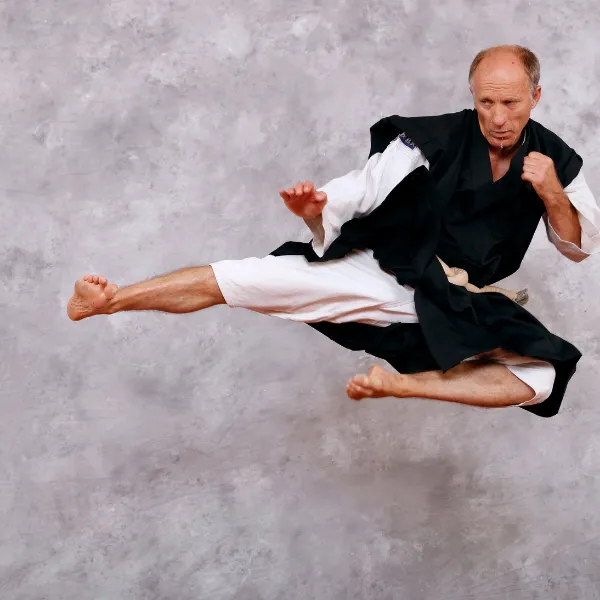 Martial artist in mid-air, performing a high kick against a gray textured background, wearing traditional black and white attire.