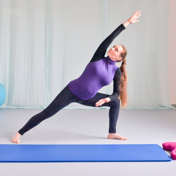 A woman in a purple top and black leggings practices a side angle yoga pose on a blue mat in a serene, softly lit room.