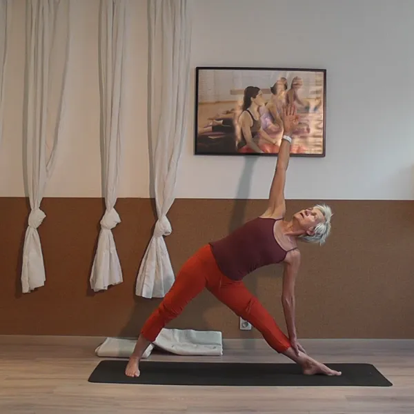 Person practicing yoga in a triangle pose on a mat, in a room with hanging white curtains and a framed picture on the wall.