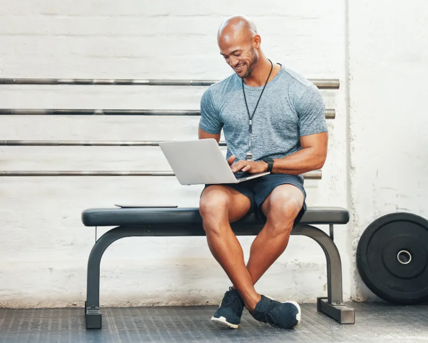 Mann in Sportkleidung sitz indoor und arbeitet am PC mit dem Eversports Manager