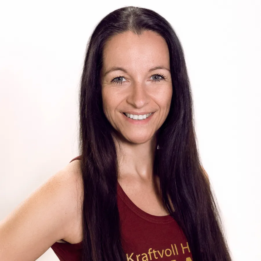 A woman with long dark hair smiles, wearing a sleeveless maroon top, against a plain white background.