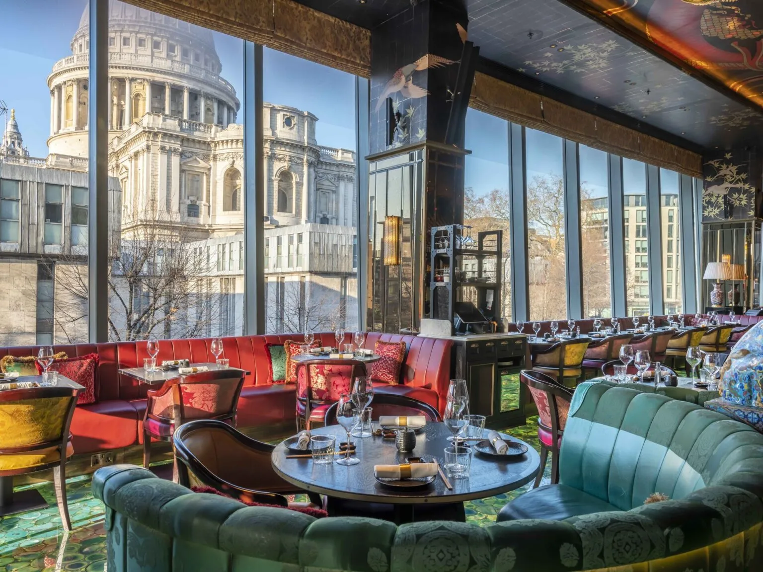 Luxurious restaurant interior with colorful seating, set dining tables, and large windows offering a view of St Paul's Cathedral dome.