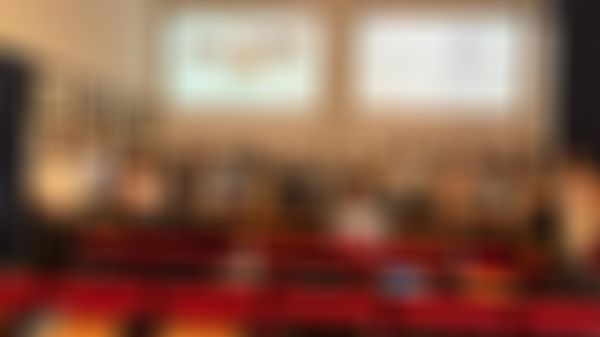 A group of people pose in a conference room, with a presentation screen and several framed portraits on the walls.