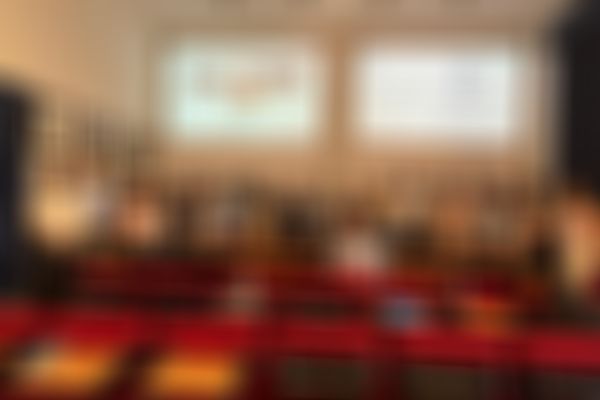 A group of people pose in a conference room, with a presentation screen and several framed portraits on the walls.