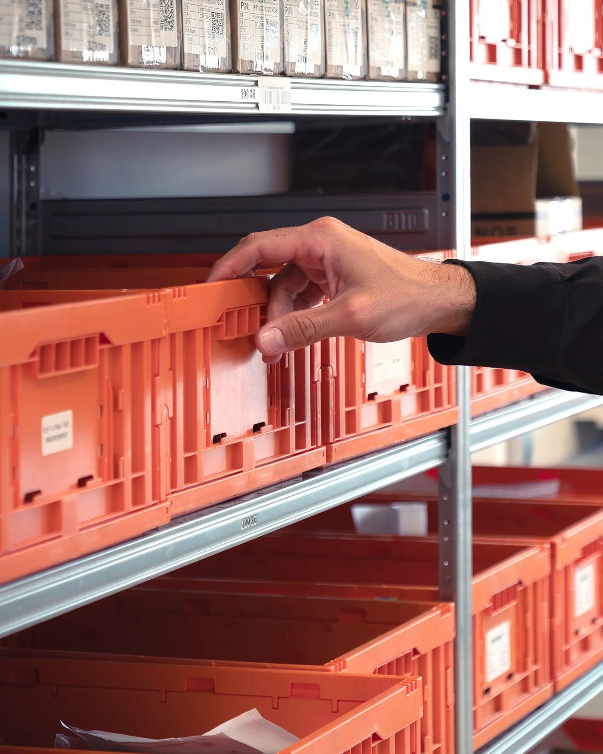 Mitarbeiter aus der Logistikabteilung greift zu einer Versandkiste aus einem Regal mit diversen Versandkisten