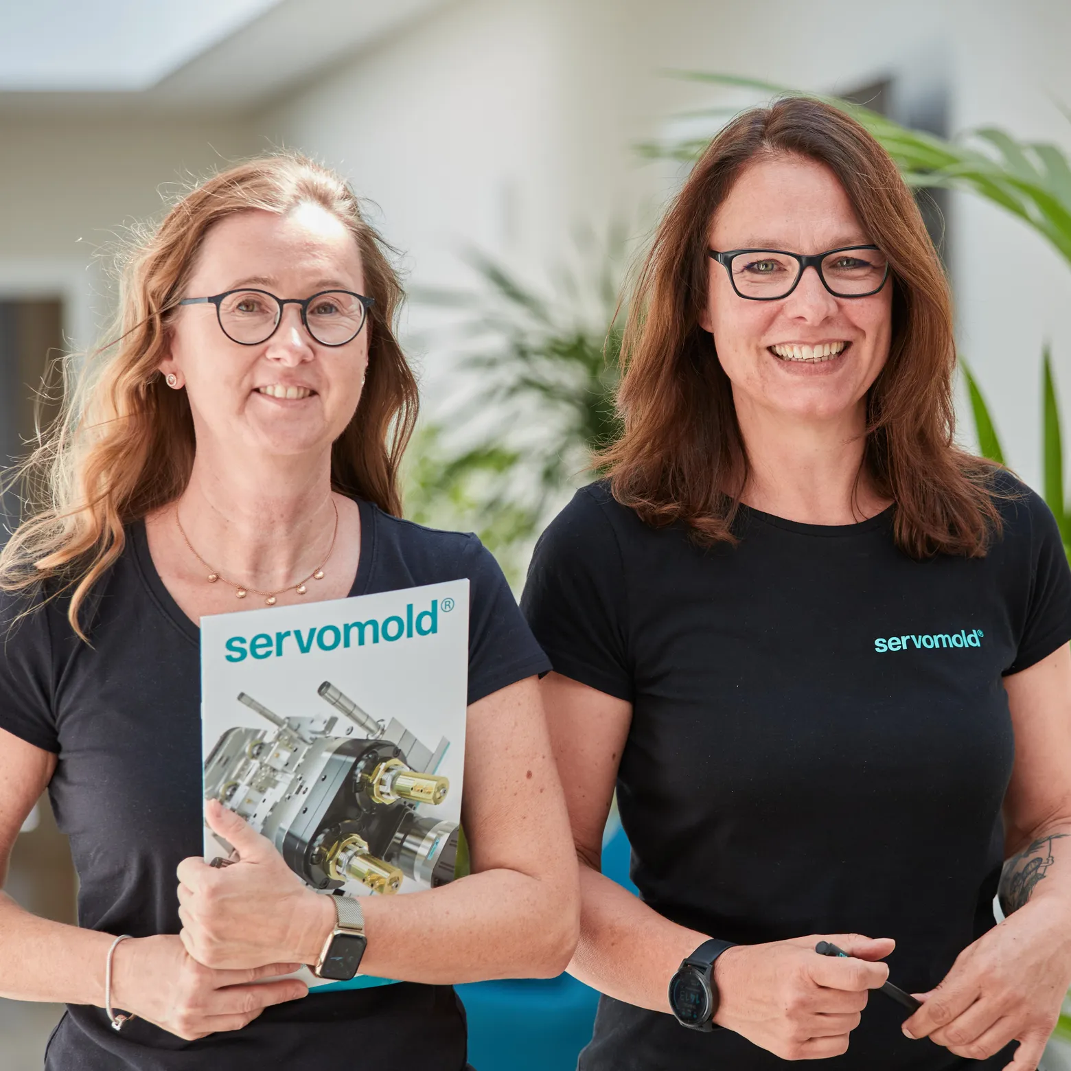 geschäftsführerin und mitarbeiterin im flur mit prospekten in der hand