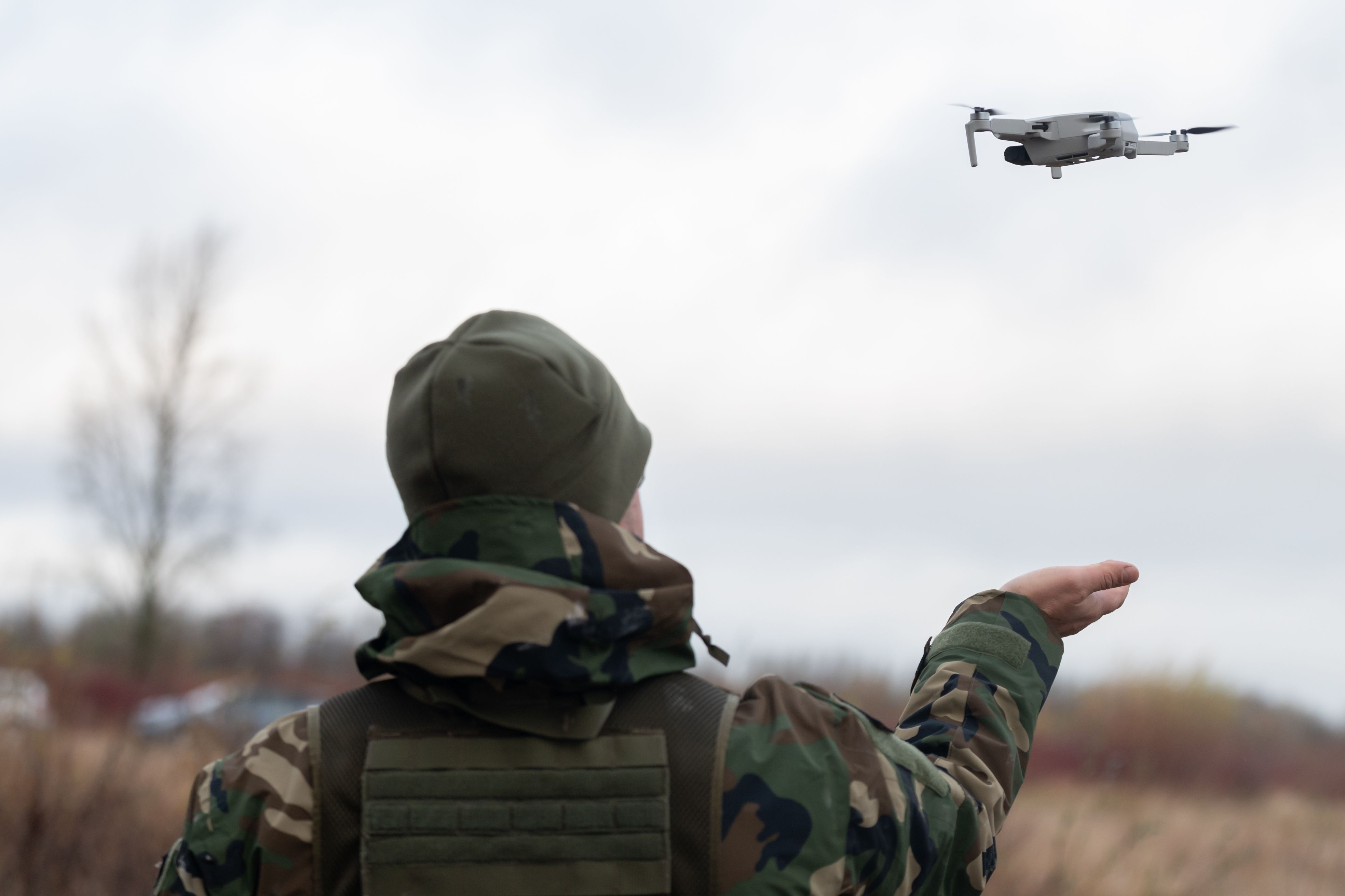 Soldier in camouflage gear operating a small drone in the field