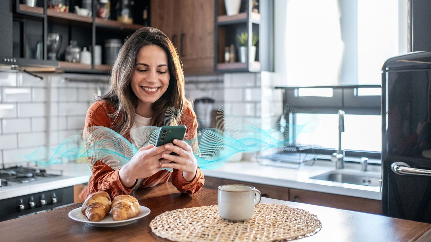Smiling woman using smartphone in a modern kitchen. Digital wave graphics around the phone.