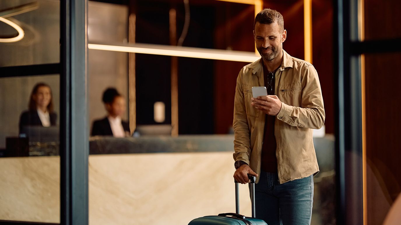 A man with a suitcase checks his phone while walking in a hotel lobby.