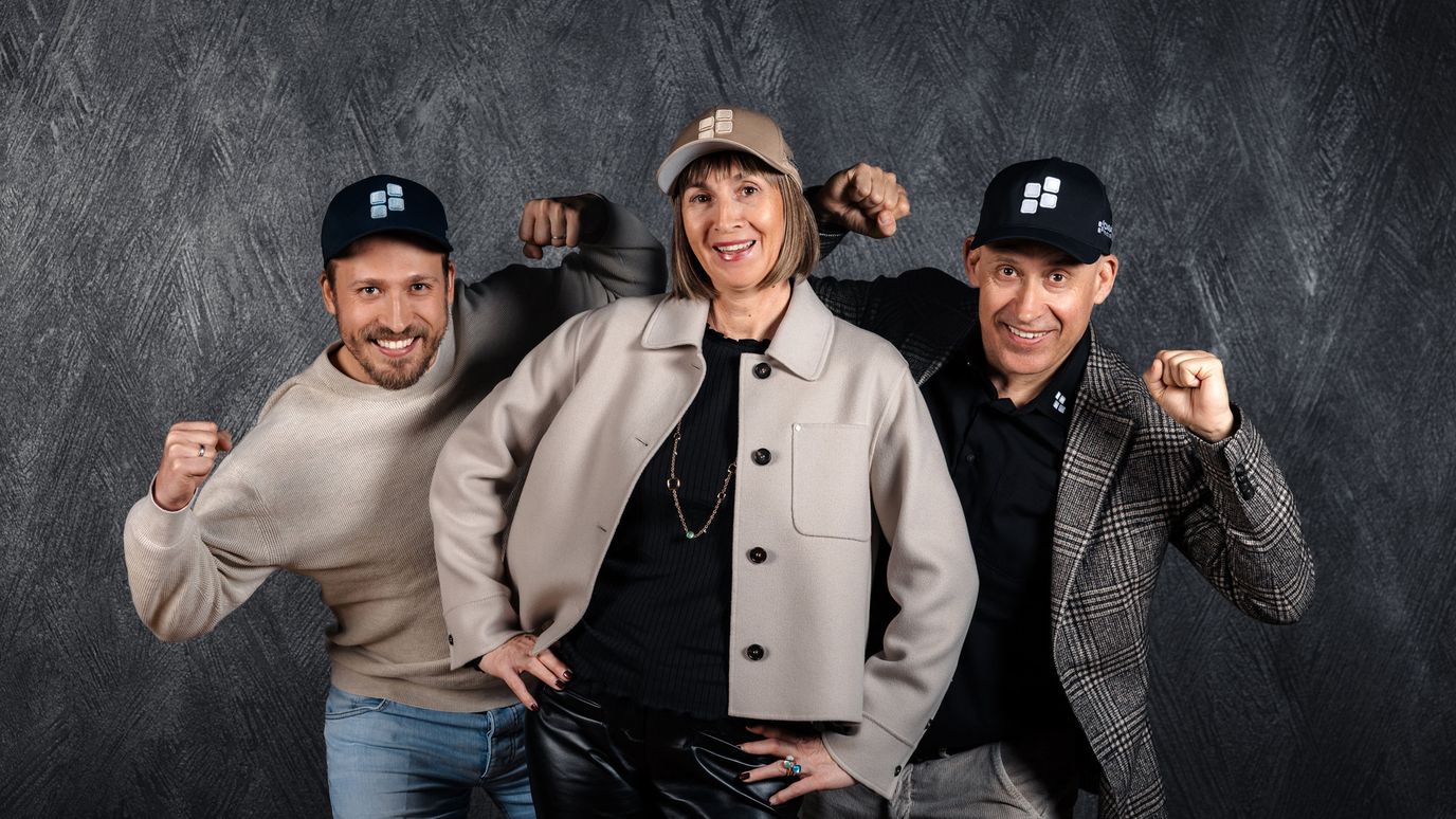 Three people wearing caps pose confidently against a textured dark background, smiling and flexing their arms.