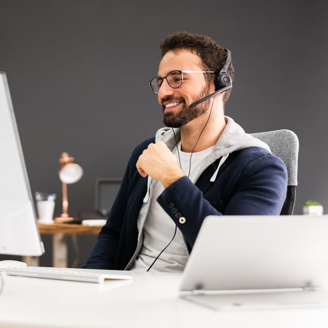 Man with glasses and headset smiling while working at a computer.