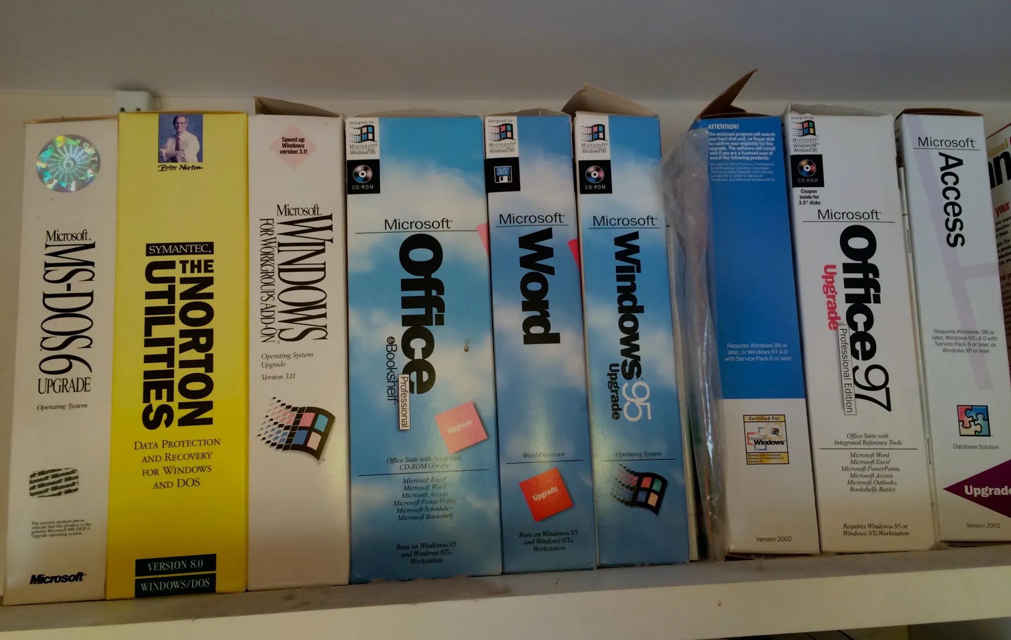 A shelf displaying vintage software boxes, including MS-DOS, Norton Utilities, Windows 95, Microsoft Office, Word, and Access.