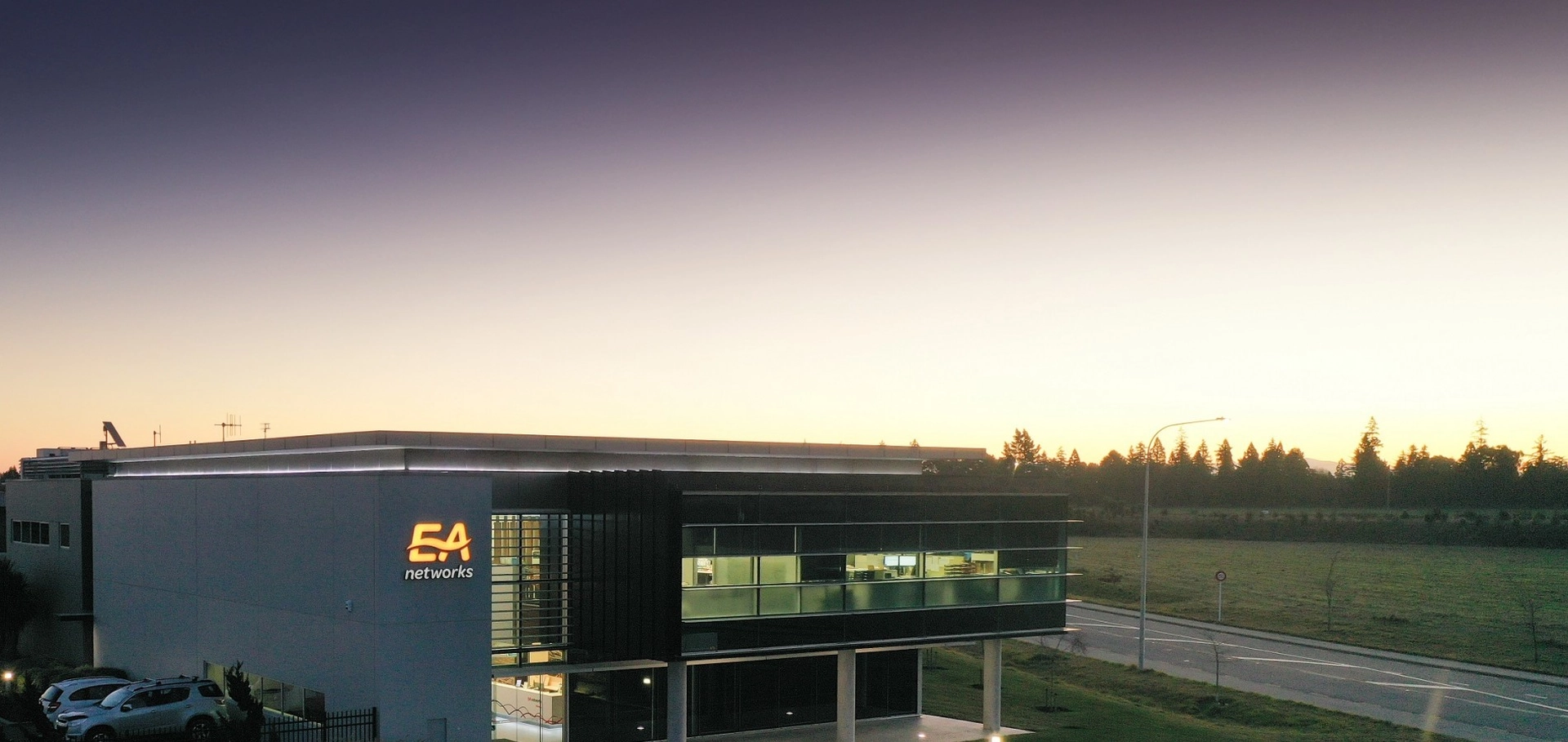 Modern building with large windows at sunset, featuring "EA Networks" logo. A road and grassy field are nearby.