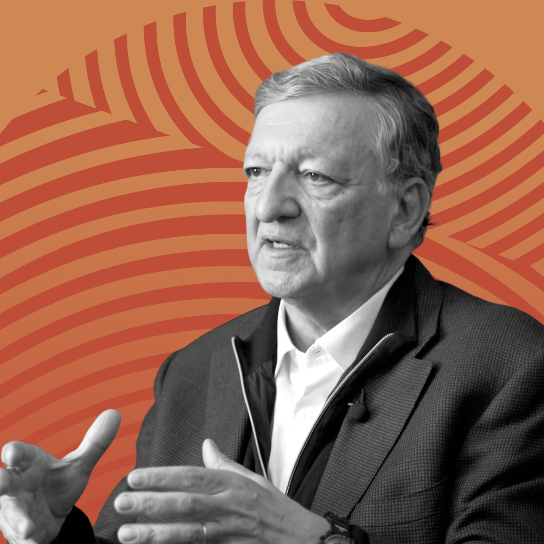 A man in gestures while speaking, set against an orange background with curved lines.