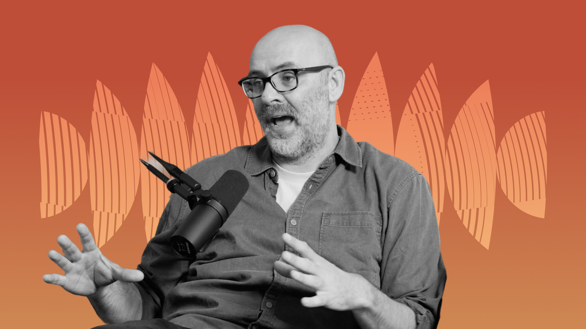 Man with glasses speaking into a microphone, gesturing with his hands, against an abstract orange background.