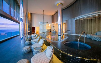 Luxurious spa with a hot tub, plush seating, and large windows offering a panoramic ocean view; modern and serene atmosphere.