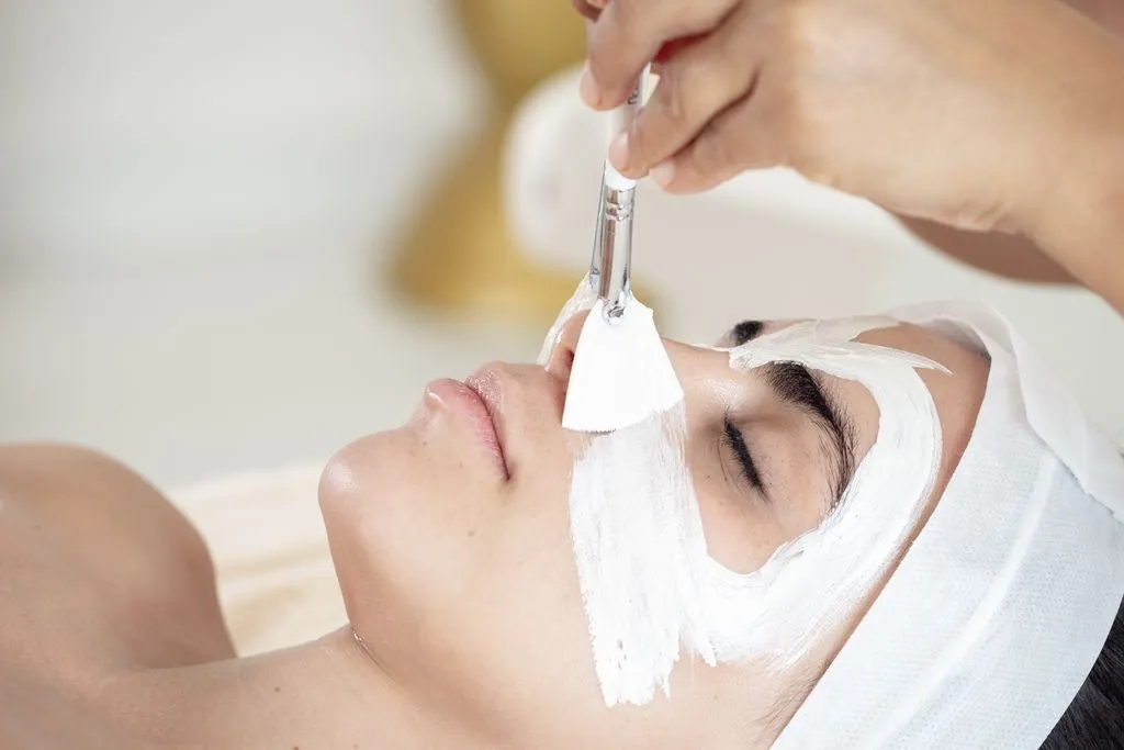 A person receiving a luxurious facial treatment, with a white mask being applied by a brush, enhancing relaxation and wellness.