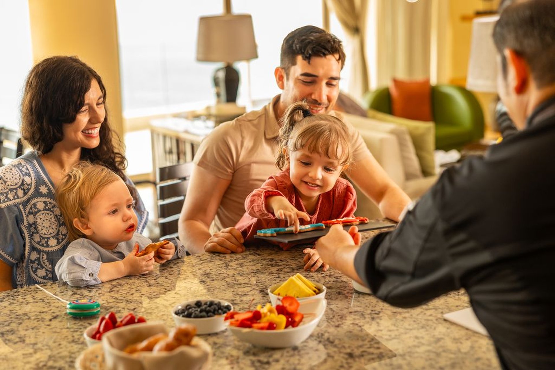 A family with two children enjoys a hands-on cooking activity in a luxurious resort setting, surrounded by fresh fruits and a cheerful atmosphere.