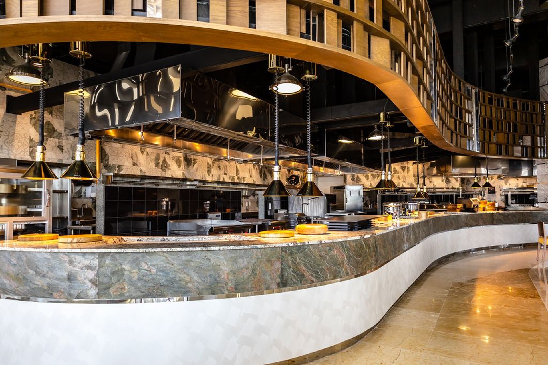 Modern, elegant restaurant interior with a curved marble counter, hanging lamps, and a wooden ceiling feature, creating a sophisticated ambiance.