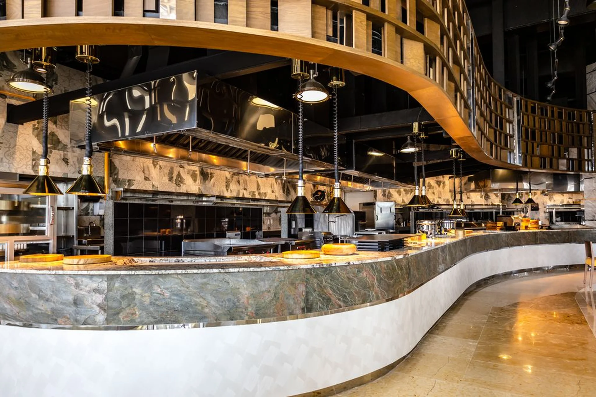 Modern, elegant restaurant interior with a curved marble counter, hanging lamps, and a wooden ceiling feature, creating a sophisticated ambiance.