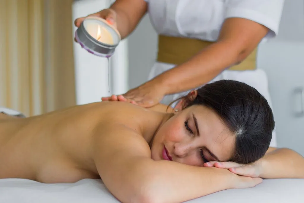 A woman enjoys a relaxing candle oil massage at a spa, lying face down with a serene expression as a therapist pours warm oil on her back.