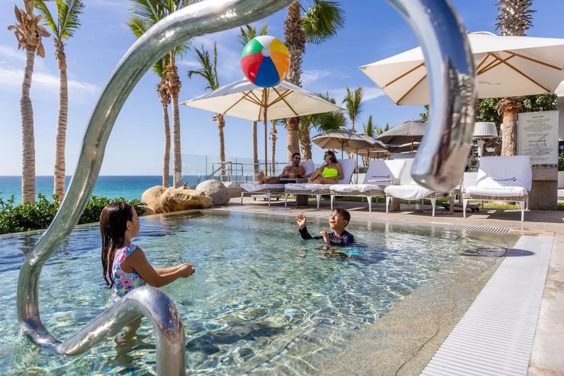 2 kids playing in the pool and the parents in the chairs