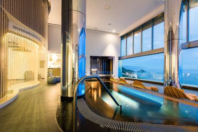 Luxurious indoor pool with a sleek design, large windows offering ocean views, and elegant seating areas illuminated by soft lighting.