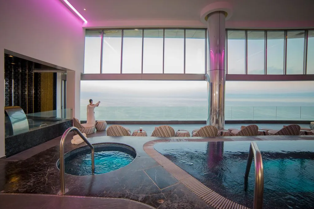 Luxurious spa with a hot tub, plush loungers, and panoramic ocean views under soft lighting; person admiring the sea.
