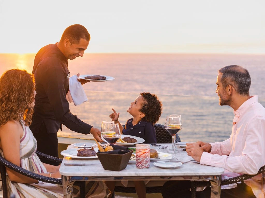 family of 3 dining at a oceanfront restaurant with a sunset view