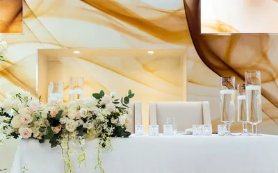Elegant wedding table with white floral centerpiece, tall glass candles, and a soft, flowing gold and white backdrop.