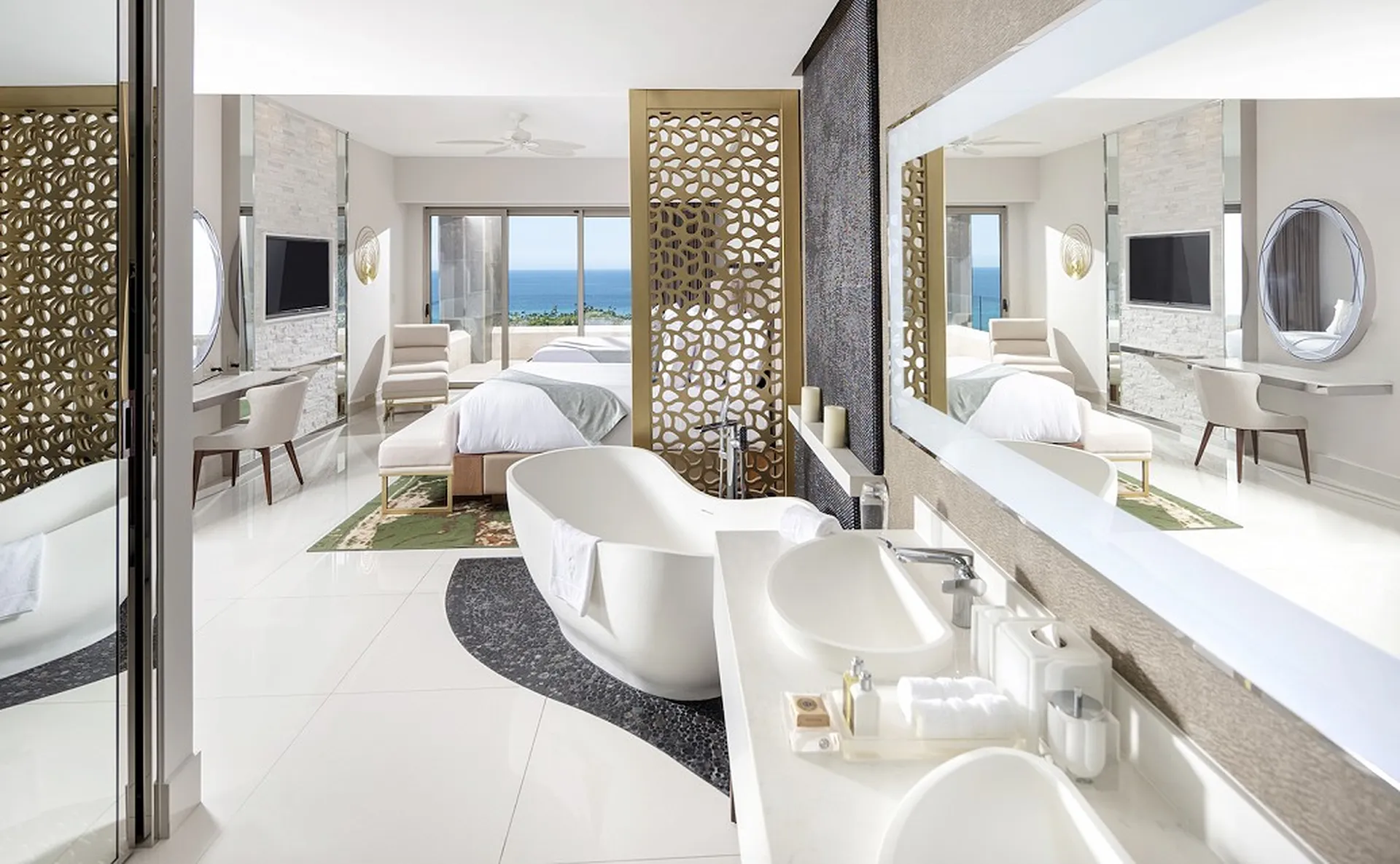 Luxurious hotel suite with ocean view, featuring a modern bathroom, double sinks, freestanding tub, and a spacious bedroom with elegant decor.