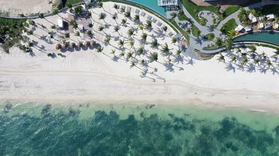 Aerial view of a pristine beach with palm trees, white sand, and turquoise water at a luxury resort in Cancun.
