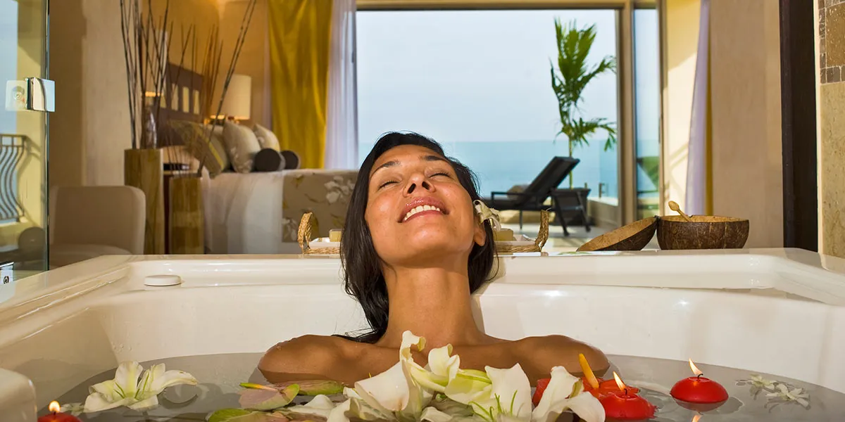 Woman relaxing in a luxurious bathtub with flowers, overlooking a beachfront view through the window.