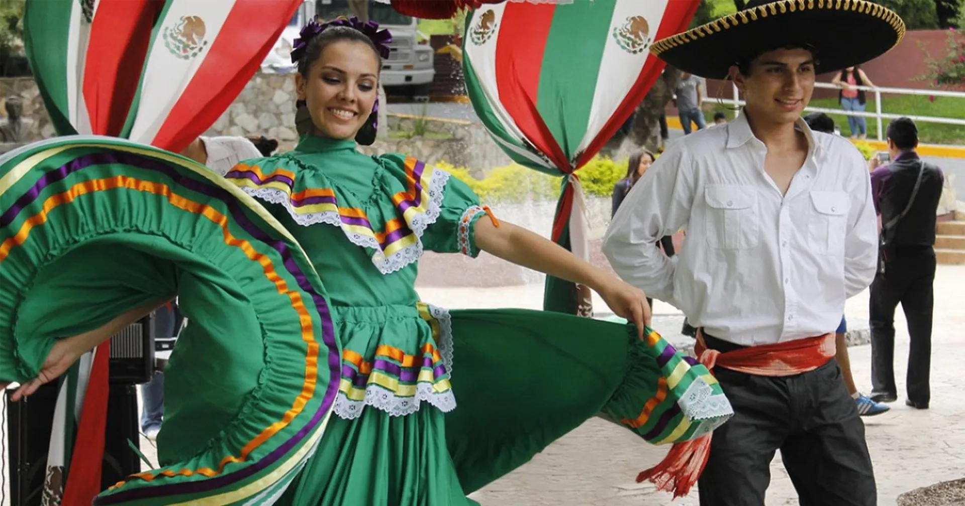 Couple performing a traditional Jalisco folk dance in a green dress and charro hat
