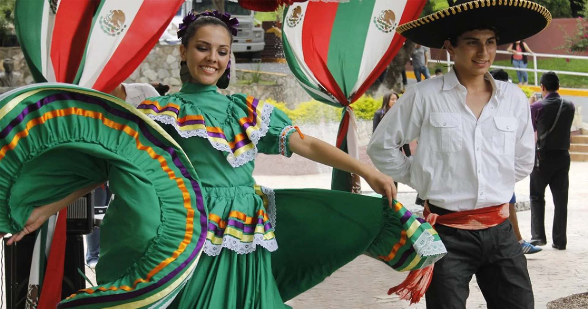 Couple performing a traditional Jalisco folk dance in a green dress and charro hat