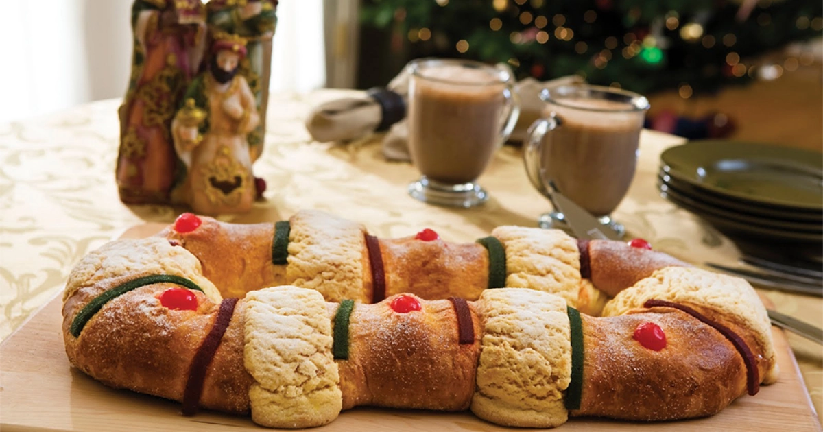 Rosca de Reyes (Three Kings bread) with candied fruit next to mugs of hot chocolate