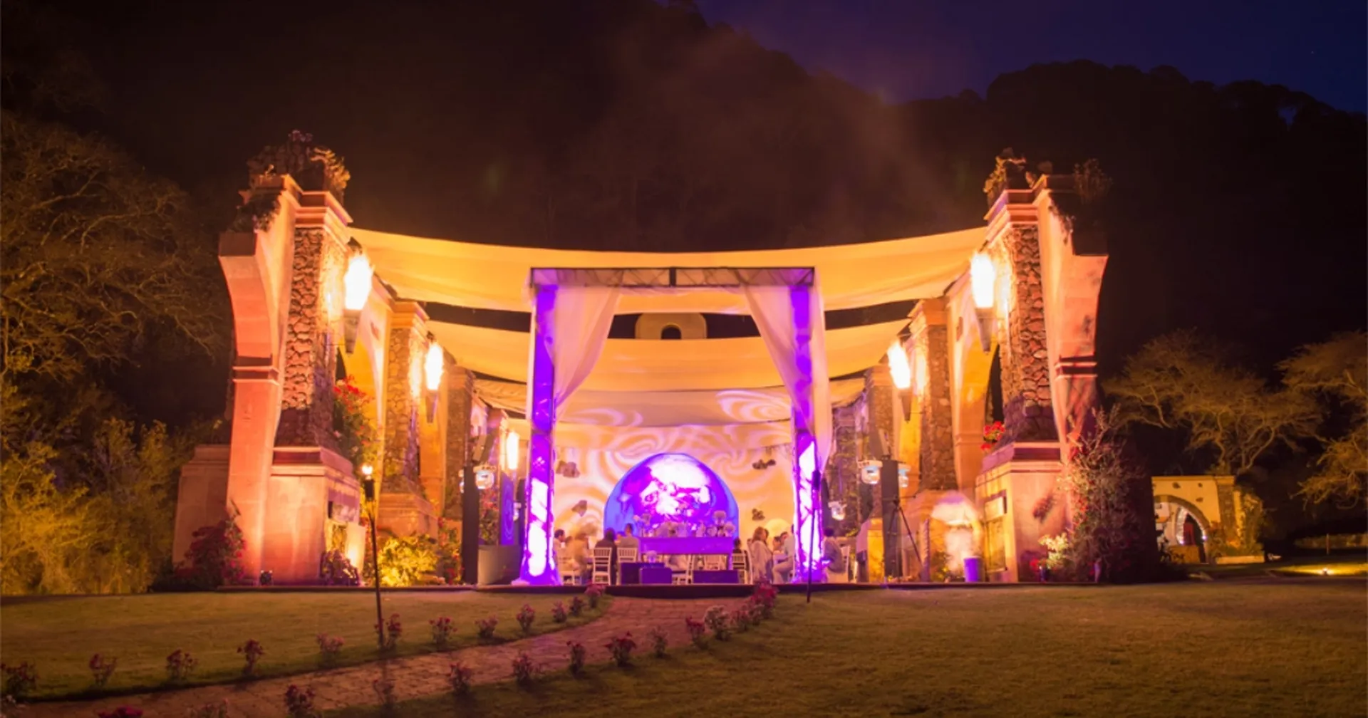 Nighttime wedding reception under a lit canopy between stone arches at Sierra Lago