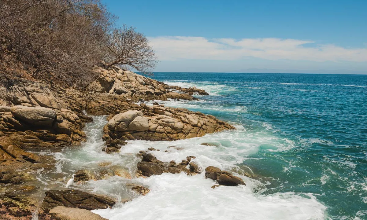 Rocky coastline with waves crashing against the shore under a clear blue sky.