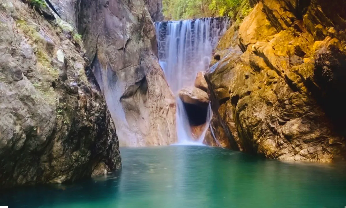 A tranquil waterfall cascades into a clear turquoise pool, surrounded by rugged cliffs and lush greenery.
