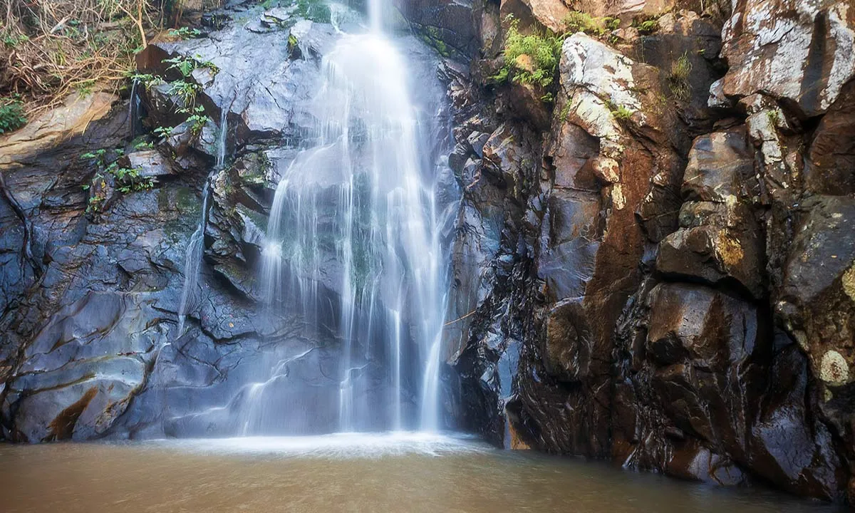 A tranquil waterfall cascading over rocky cliffs into a serene pool, surrounded by lush greenery.