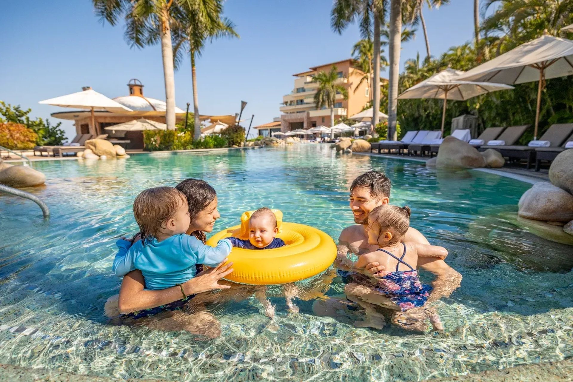 A joyful family enjoys swimming together in a luxury resort pool, surrounded by lush palm trees and scenic views.