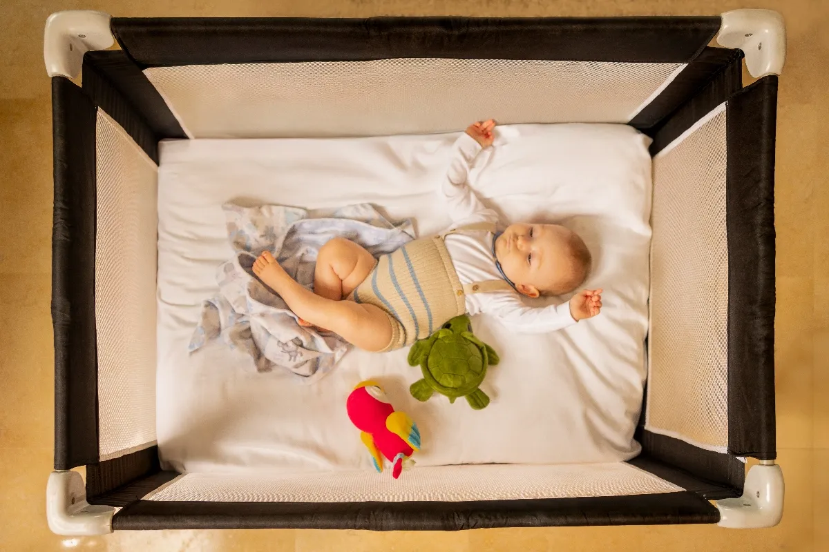 Baby peacefully sleeping in a crib with a green turtle toy and colorful plush toy, wearing a striped outfit.