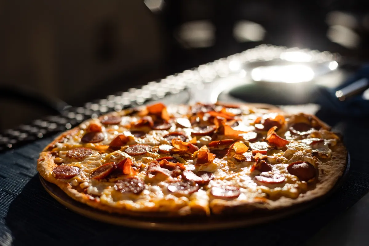 Pizza topped with pepperoni and bacon on a wooden board, illuminated warmly by sunlight.