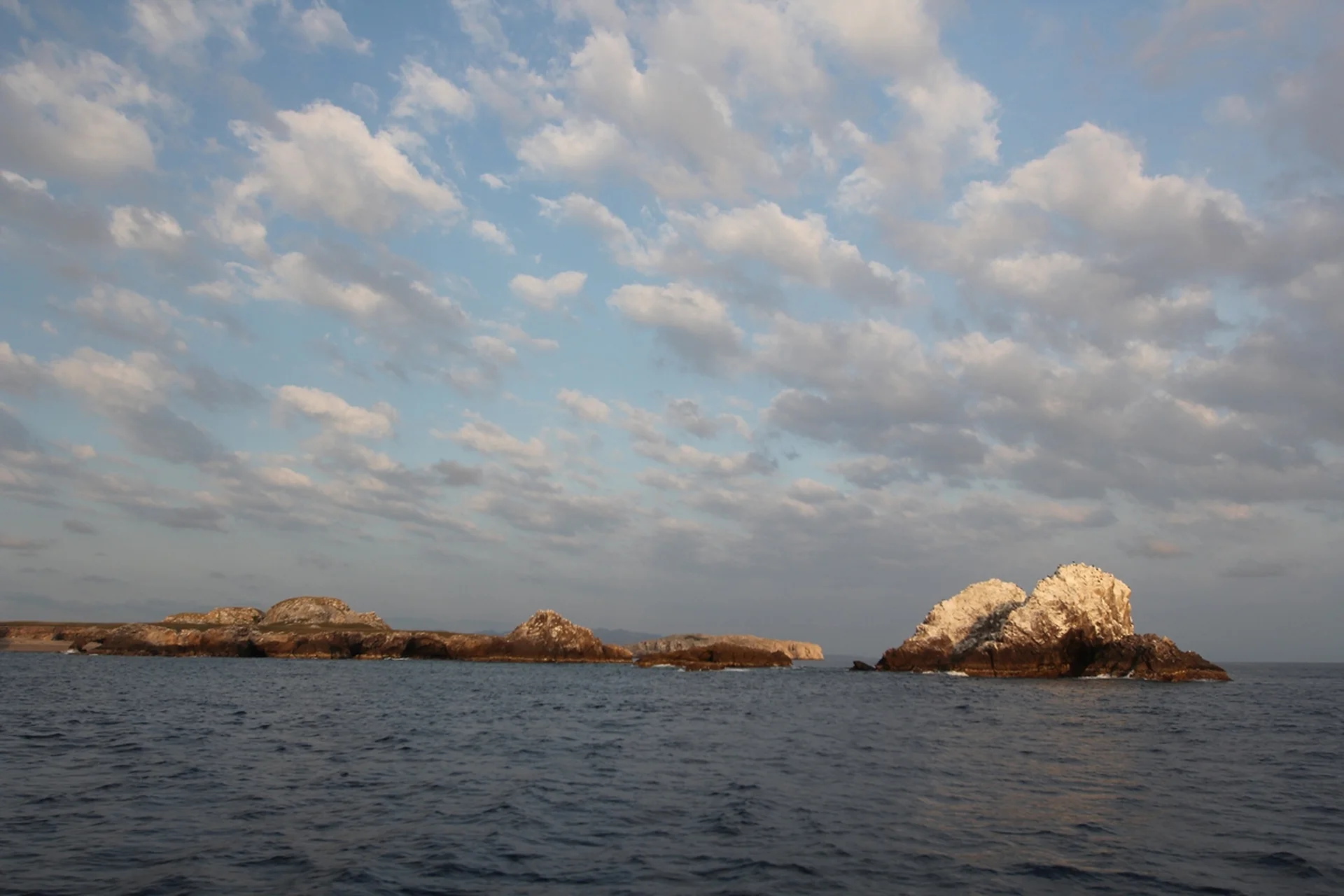 Cloudy sky over rocky islands surrounded by calm ocean waters at dusk.