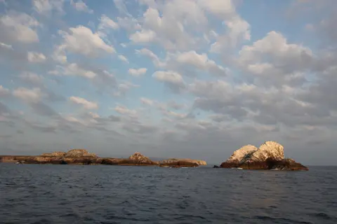 Cloudy sky over rocky islands surrounded by calm ocean waters at dusk.